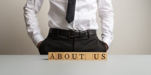 Businessman standing at a desk with About us sign assembled with wooden cubes on it.